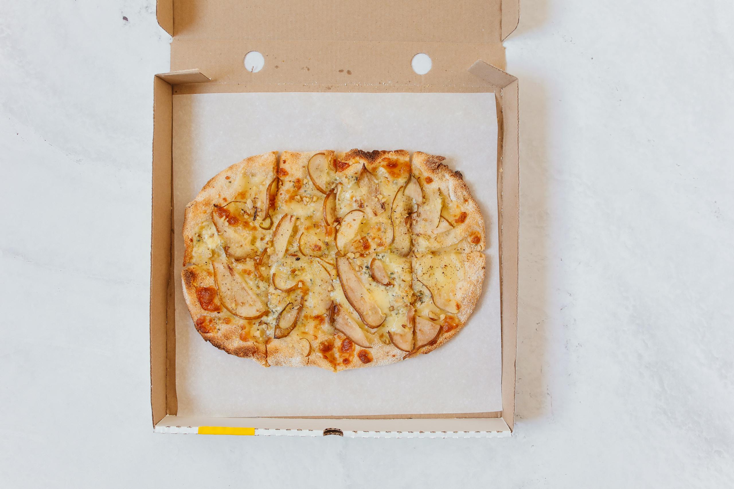 Delicious gourmet pizza topped with pears and cheese in an open takeaway box.