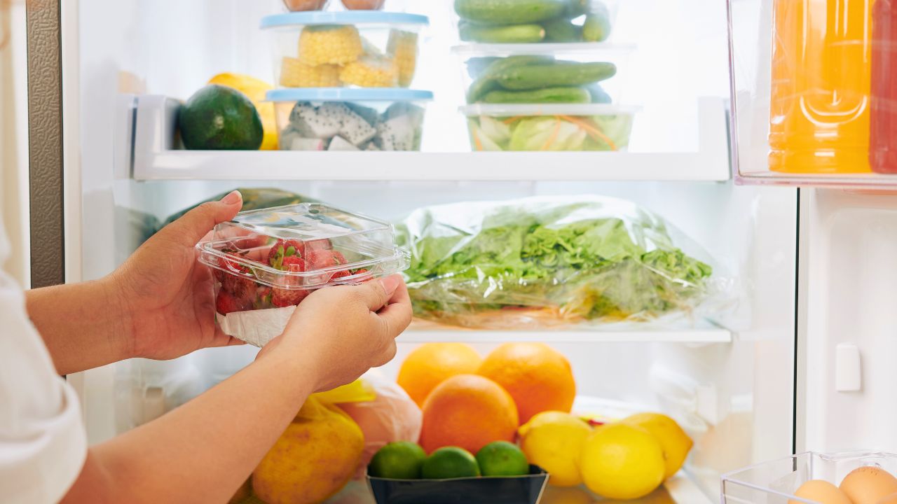 Hands placing a container of strawberries into a neatly stocked refrigerator.