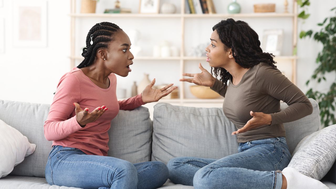 Two women sitting on a couch arguing in a bright living room.