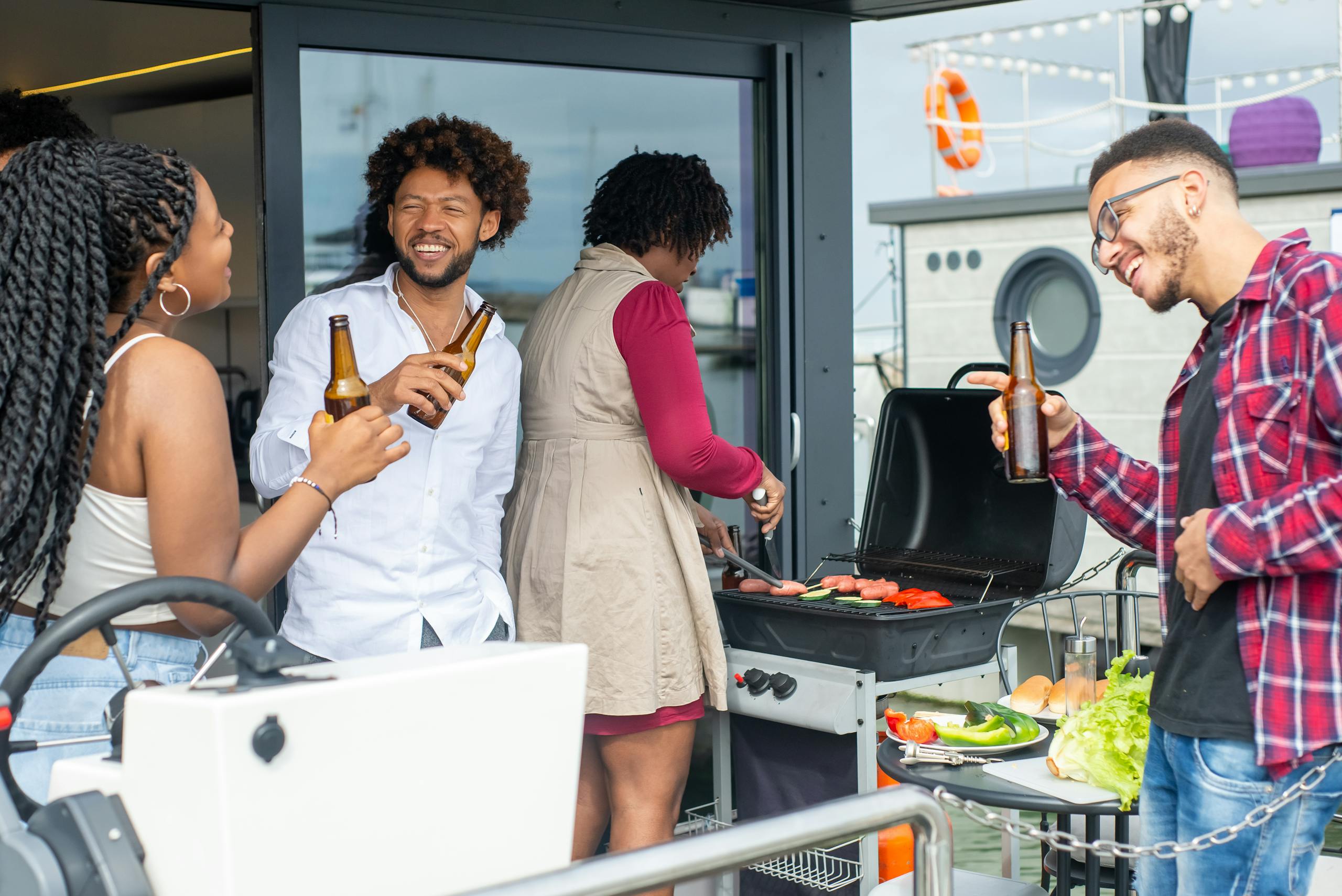 Group of friends having fun at an outdoor barbecue with drinks and smiles.