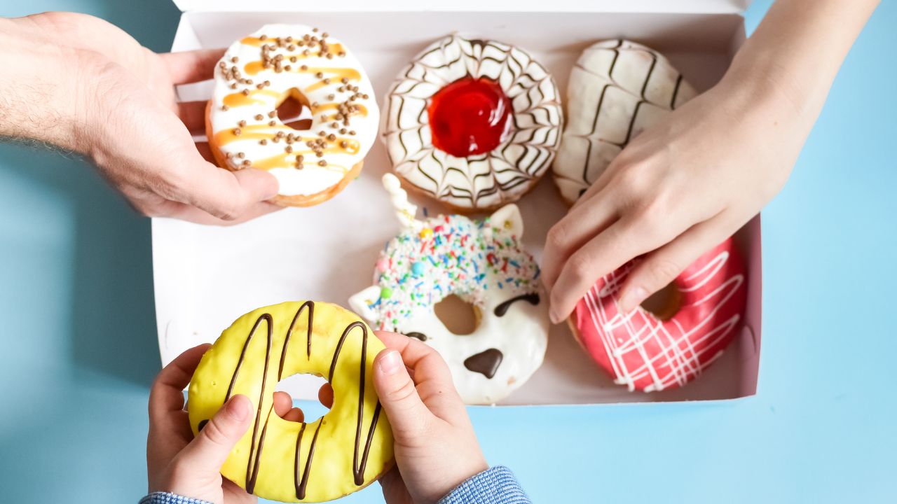 Hands reaching into a box of colorful frosted donuts.
