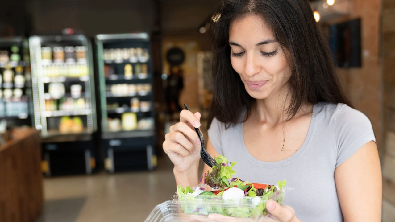 A woman eating a salad from a takeout container in a cafe.