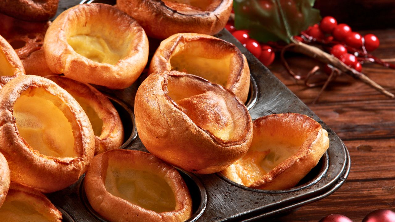 Golden Yorkshire puddings baked in a metal muffin tin on a wooden table.