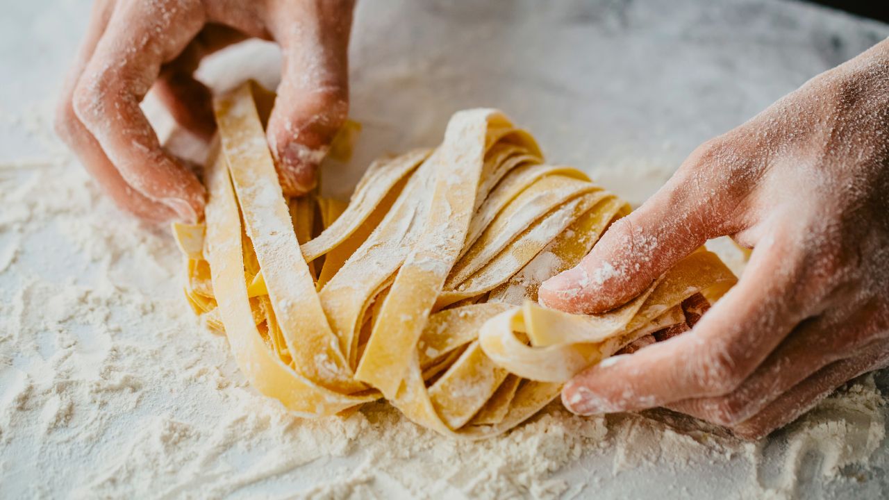 Flour-dusted hands handling fresh homemade pasta on a floured surface.