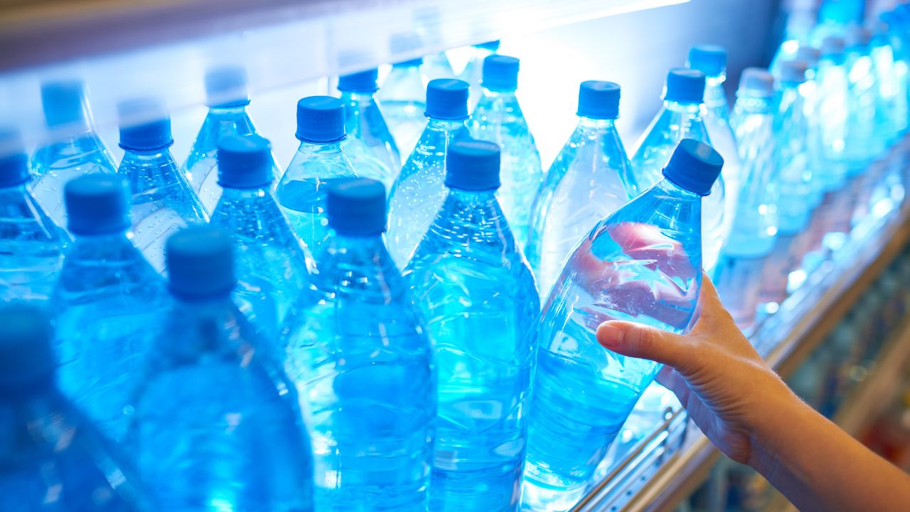 A child’s hand picking up a plastic water bottle from a store display.
