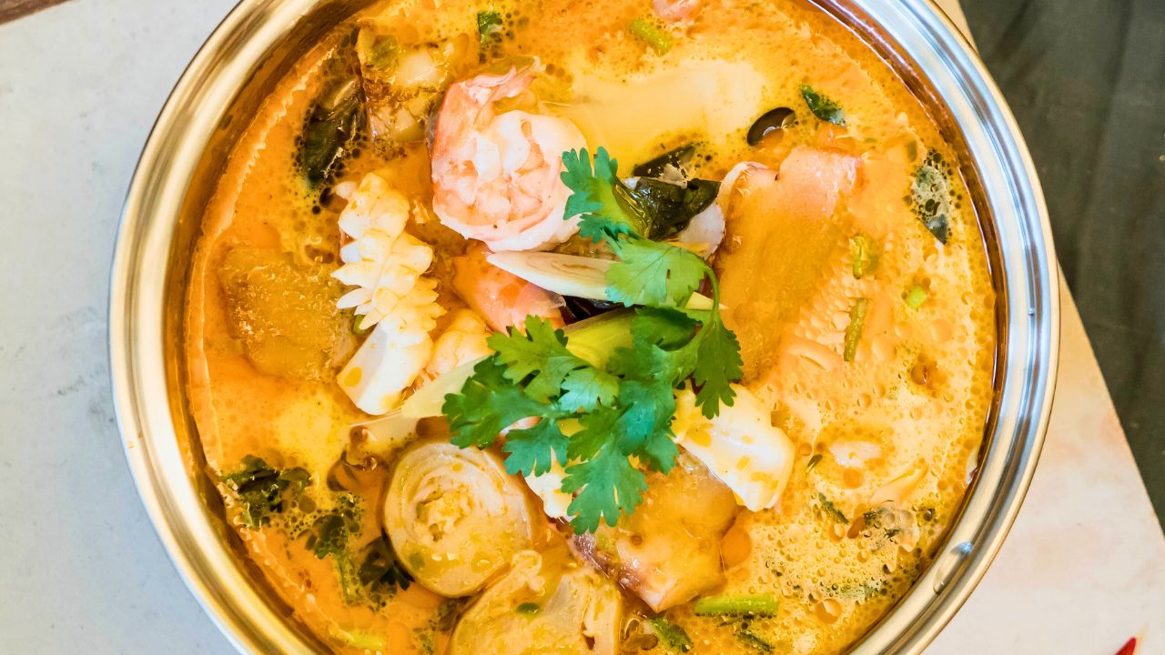 A bowl of creamy seafood soup topped with cilantro and shrimp.