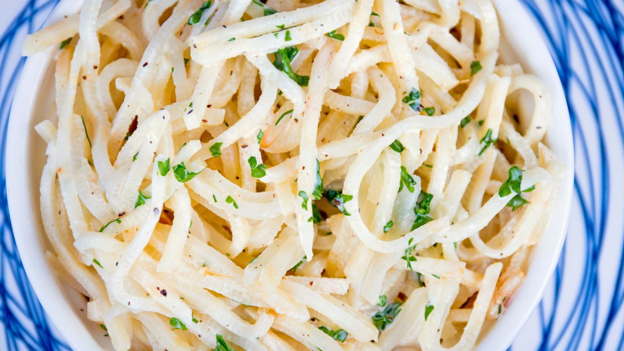 A bowl of plain pasta noodles garnished with chopped herbs.