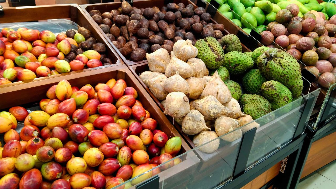A grocery display of mangoes, avocados, root vegetables, and tropical fruits.