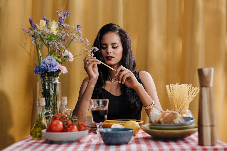 Elegant woman at a table with pasta, flowers, and wine, enjoying an Italian meal.