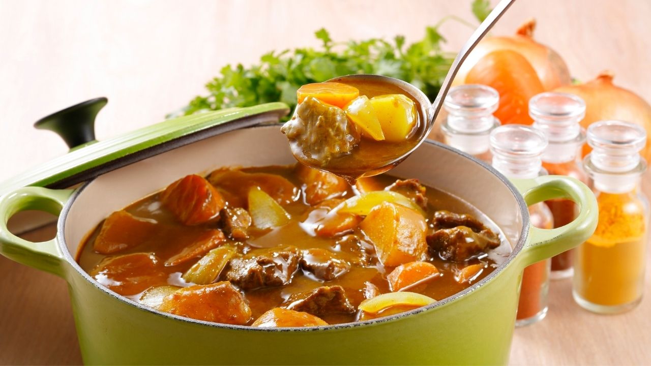 A ladle lifts beef and vegetable stew from a green Dutch oven.
