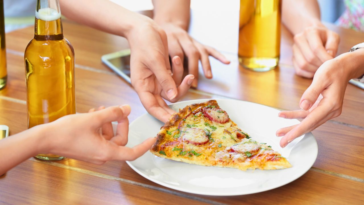 Several hands reaching for a slice of pizza on a plate at a wooden table.