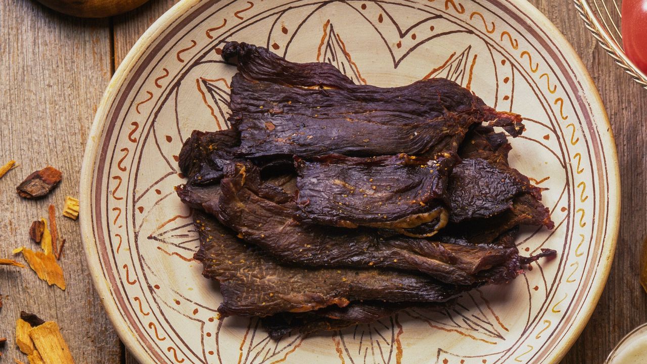 A stack of dark roasted meat on a decorative ceramic plate on a wooden table.
