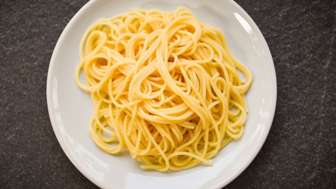 A plate of plain spaghetti on a dark countertop.