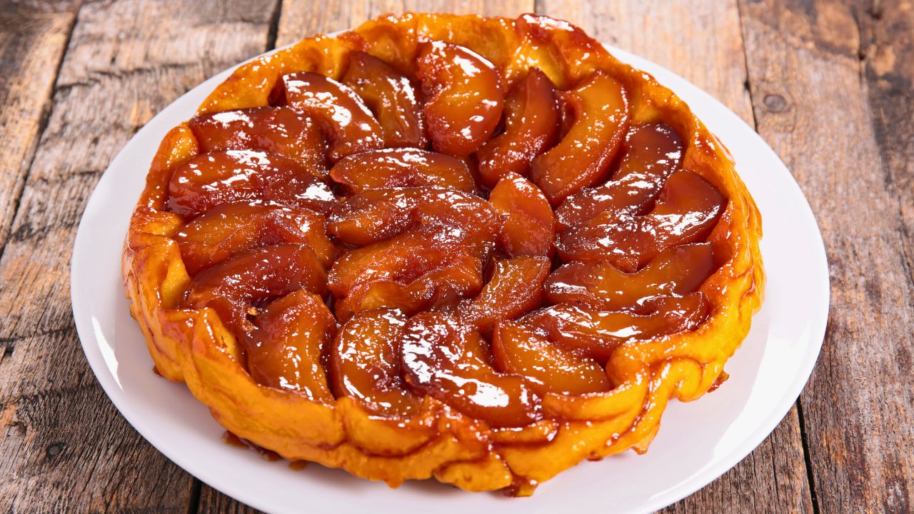 A caramelized apple tart on a white plate on a wooden table.