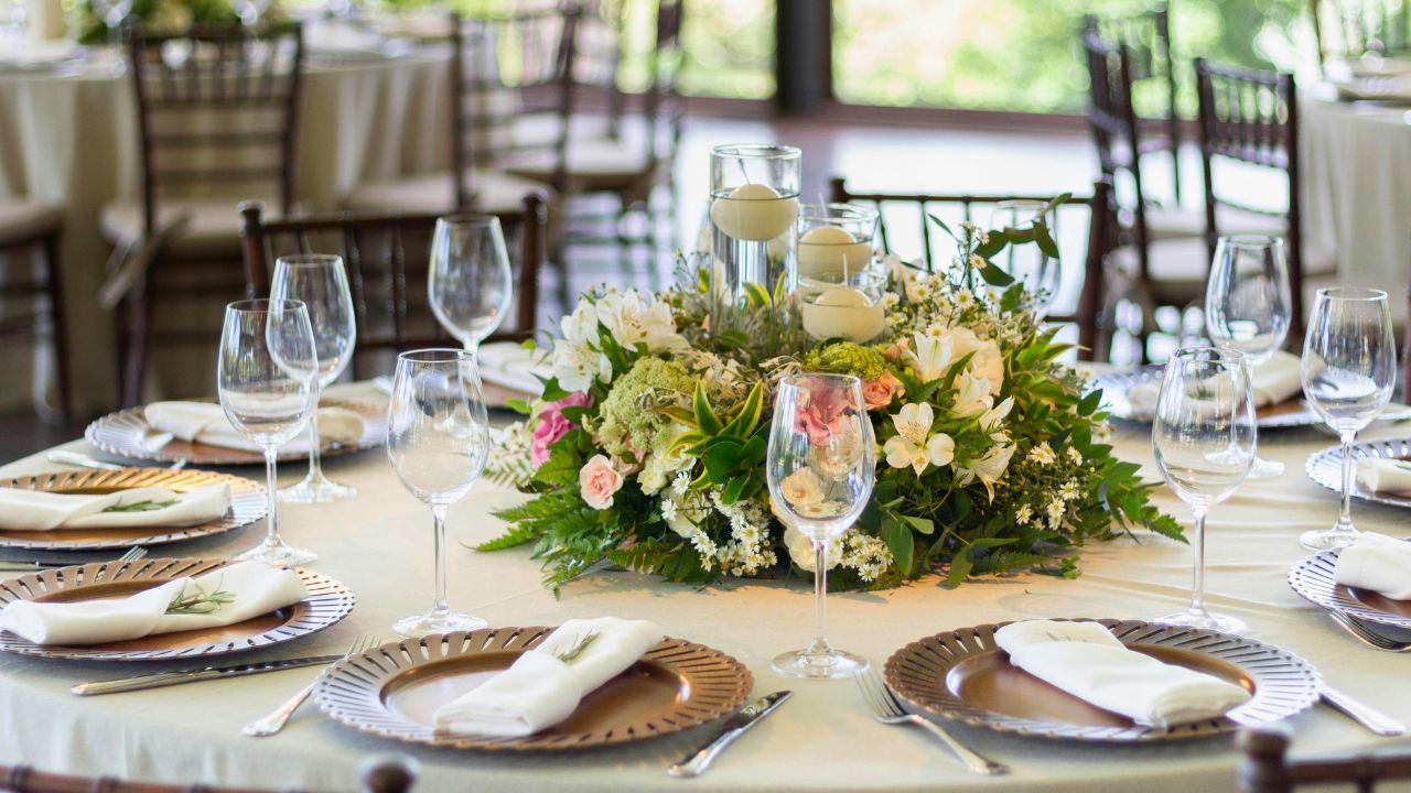 A formal dining table set with wine glasses, napkins, and a floral centerpiece.