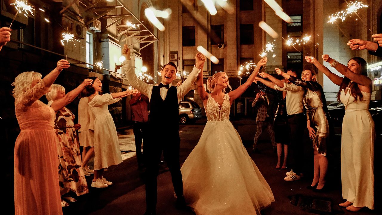 A bride and groom stand under a tunnel of sparklers on a city street at night.