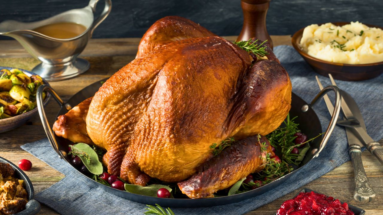 A roasted turkey on a serving platter surrounded by mashed potatoes, gravy, and cranberry sauce.