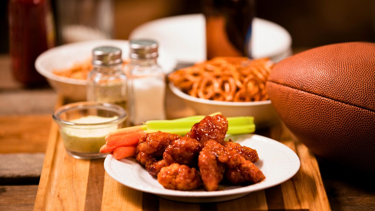 Chicken wings with celery, carrots, dip, and a football on a wooden table.