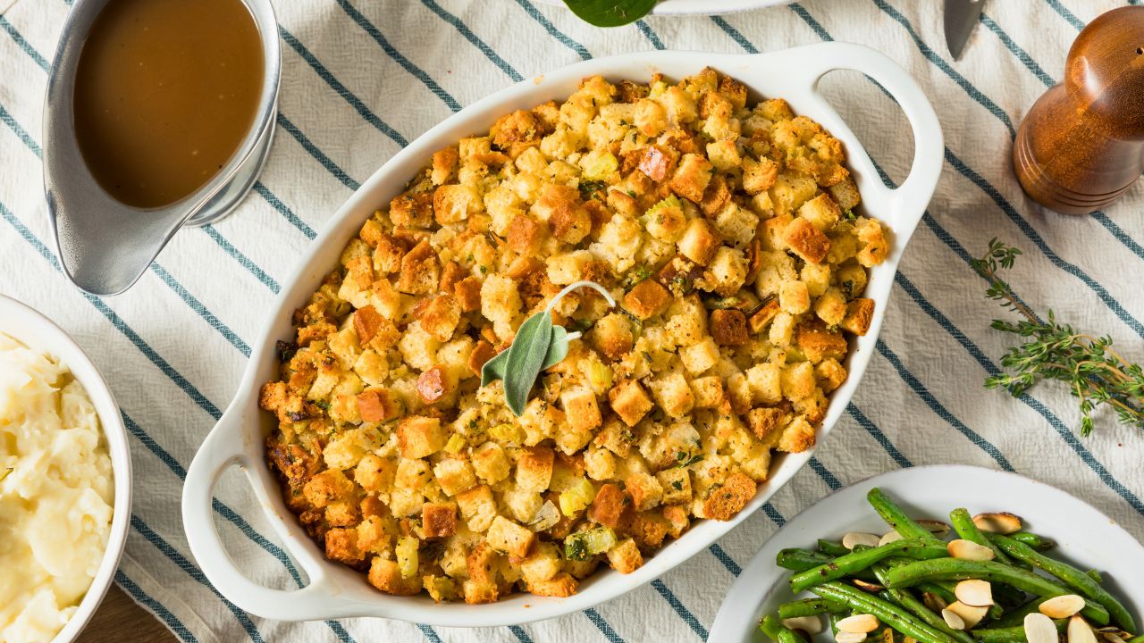 A casserole dish of stuffing on a table with gravy, mashed potatoes, and green beans.