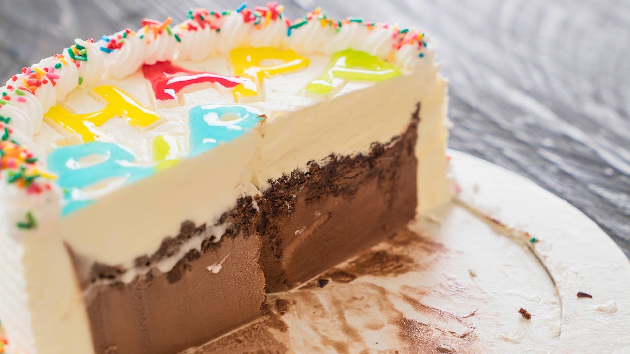 Partially sliced birthday cake with white frosting, sprinkles, and chocolate filling on a white plate.