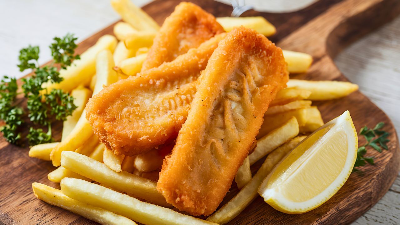 Fried fish fillets served with French fries, parsley, and a lemon wedge on a wooden board.