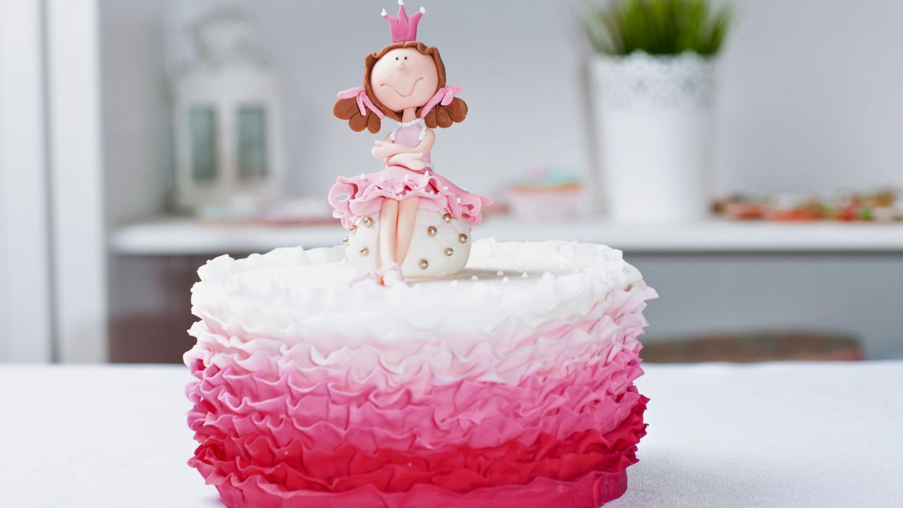 A pink-and-white princess birthday cake with a figurine topper on a white table.