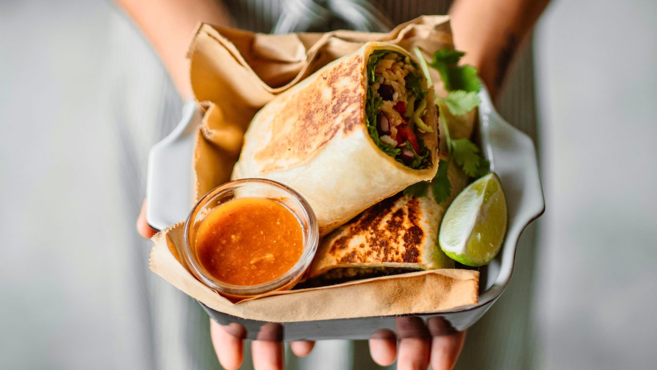 Two toasted burritos in a tray with dipping sauce and a lime wedge.