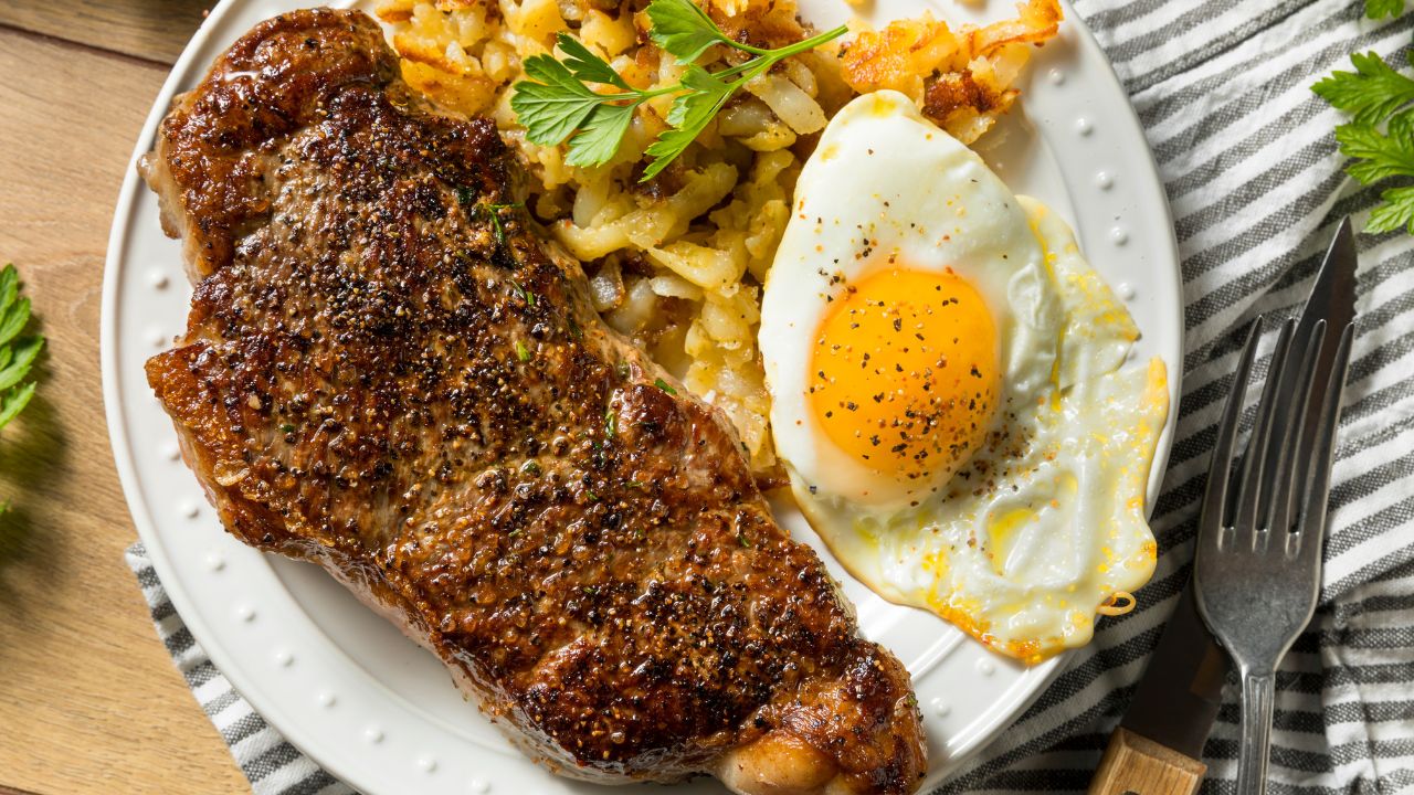 Steak, a sunny-side-up egg, and crispy potatoes on a white plate.