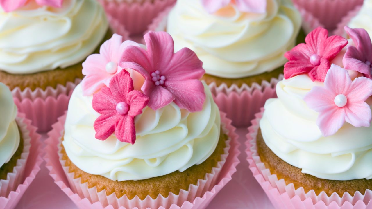 Pink and white frosted cupcakes topped with flower decorations in pink paper liners.