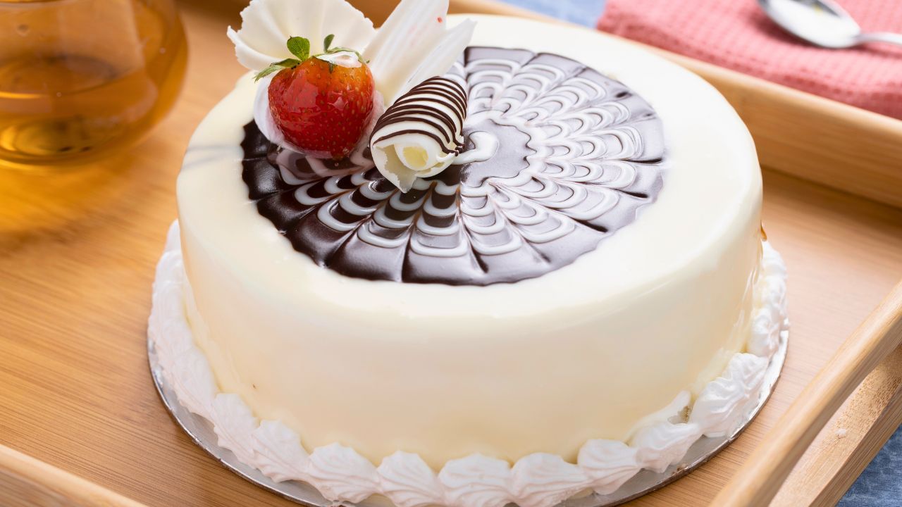A decorated white cake with chocolate swirls and a strawberry on a wooden tray.